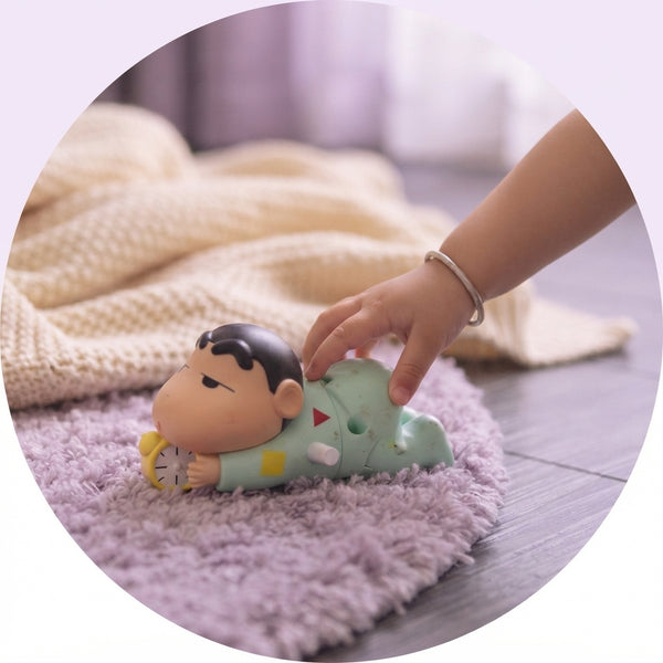 Close-up of a child reaching for a Shinchan crawling toy on a lavender rug in a cozy, softly lit room.